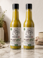 Two bottles of Smokin Bros BBQ Good Eats Green Sauce, filled with green sauce, standing on a marble countertop with a neutral background.
