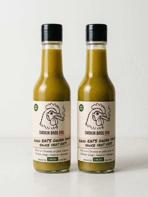 Two glass bottles of Smokin' Bros BBQ Good Eats Green Sauce, filled with a green sauce, standing side-by-side against a plain white background.