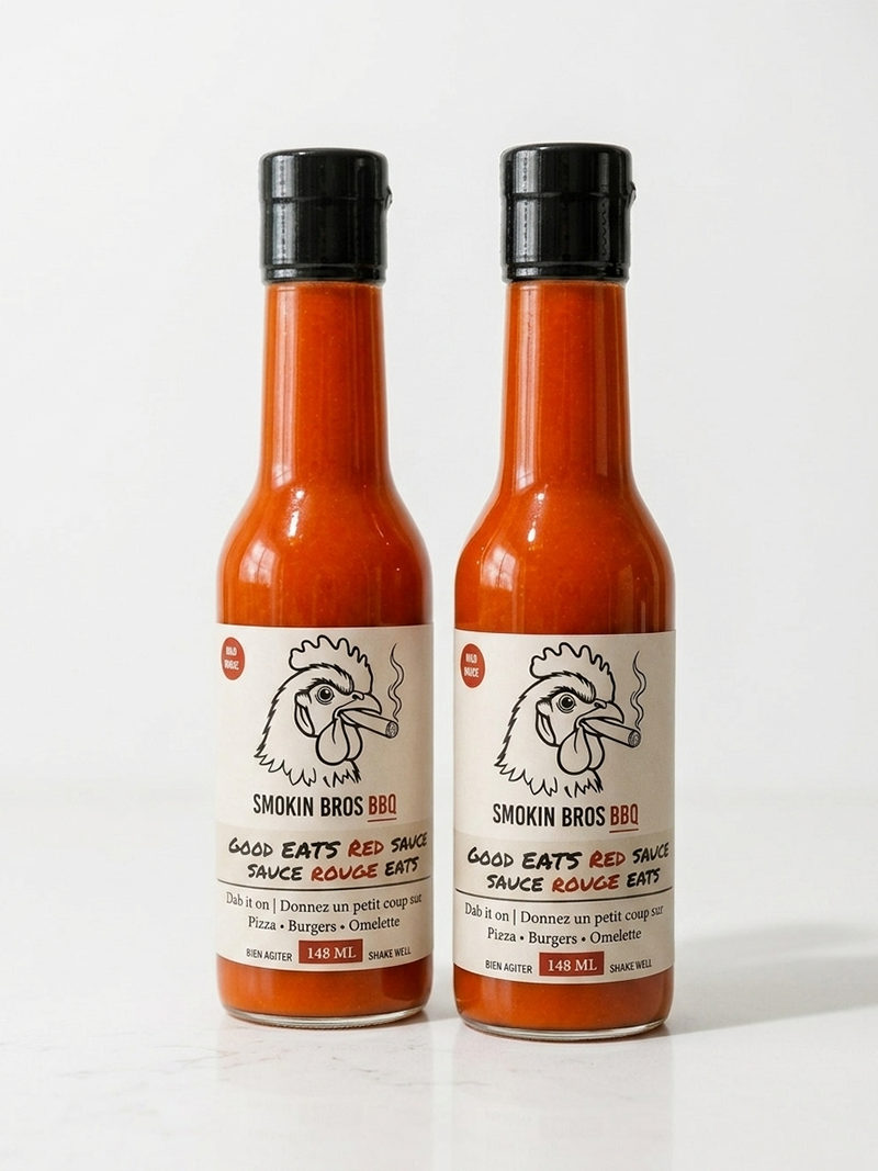 Two bottles of Smokin Bros BBQ Good Eats Red Sauce standing side by side on a white surface against a white background.