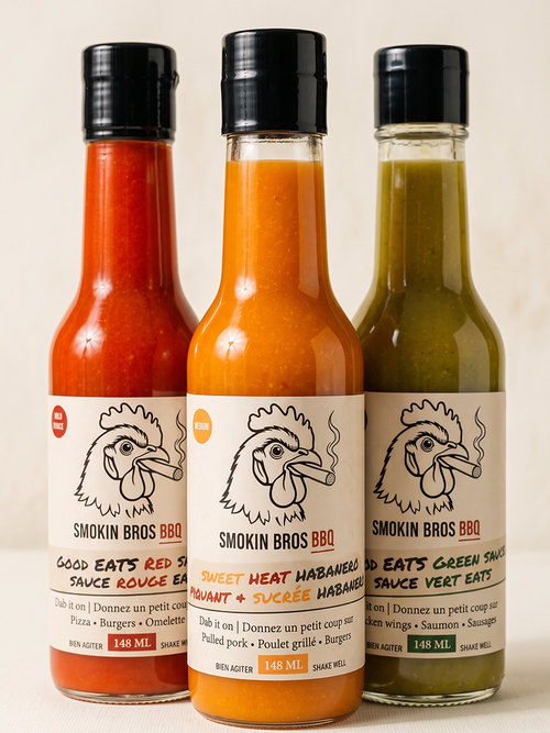 Three Smokin Bros BBQ sauce bottles standing side by side against a light beige background. The left bottle contains red sauce, the middle bottle contains orange sauce, and the right bottle contains green sauce.